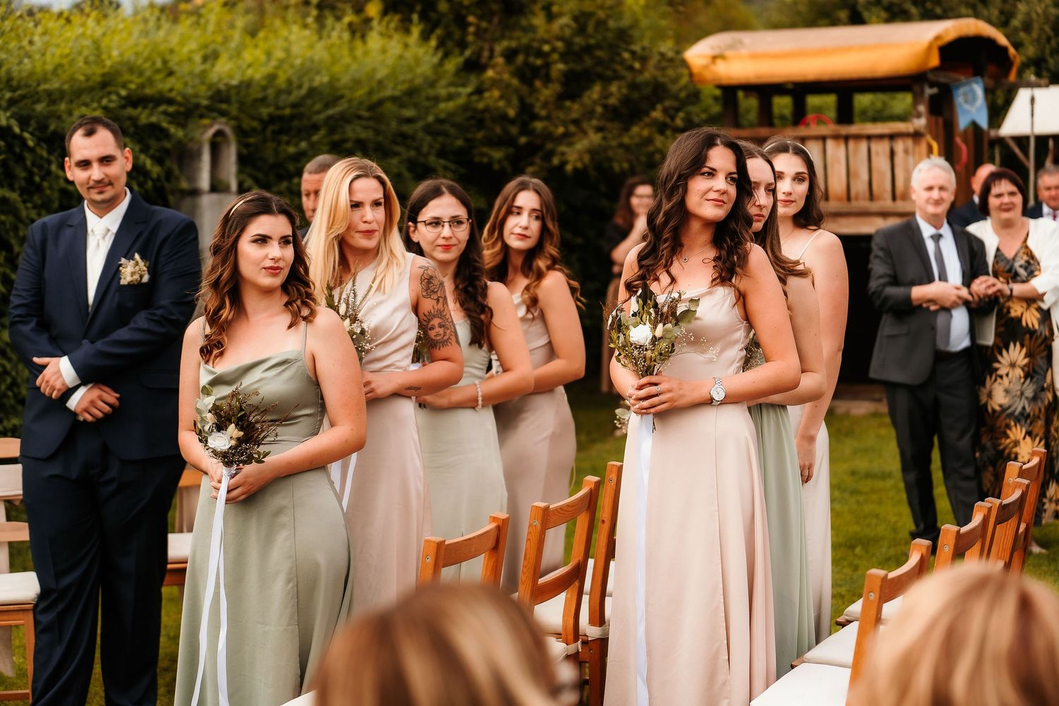 Wedding party lineup with bridesmaids in alternating sage and blush dresses outdoors.