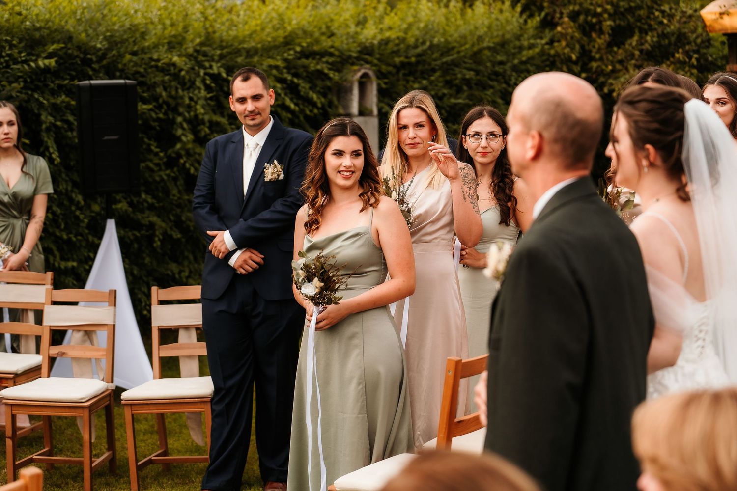 Wedding party stands at outdoor ceremony with bridesmaids in neutral dresses and groomsmen in dark suits.