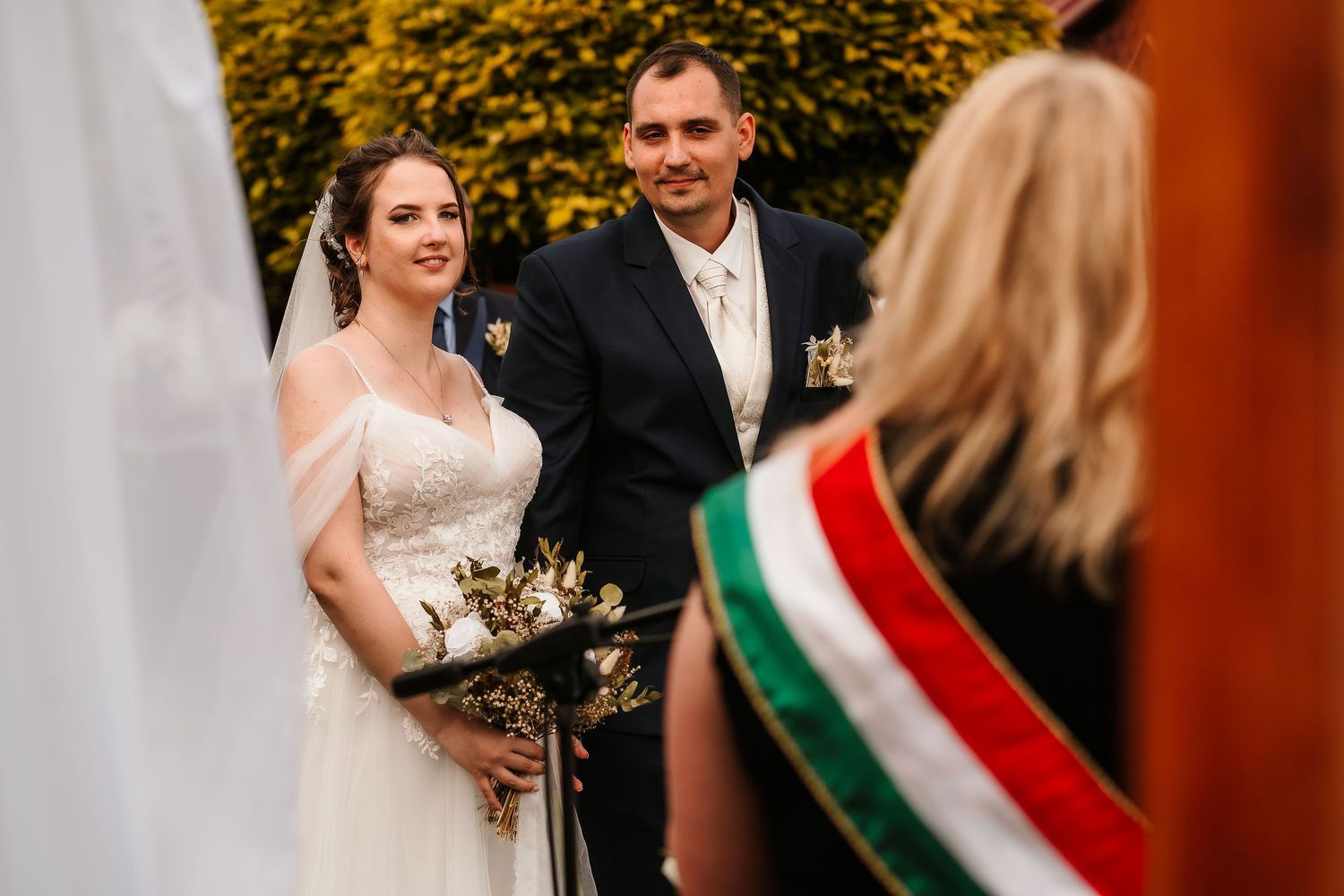 Wedding ceremony with official wearing traditional Hungarian sash conducting the service outdoors.