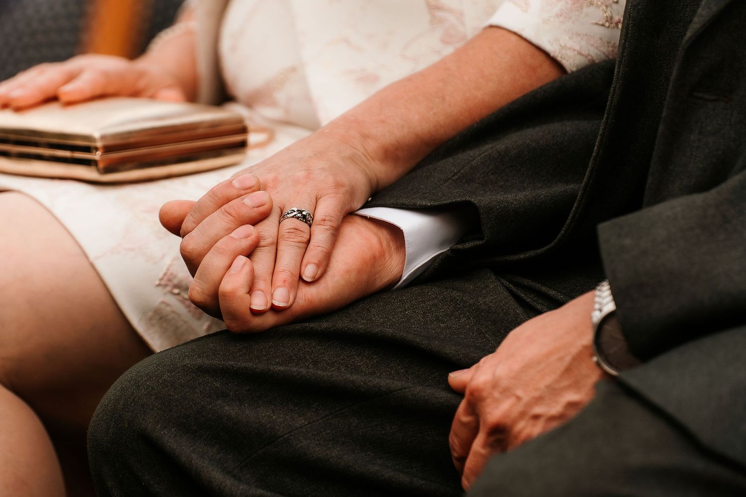 Close-up of hands holding during wedding ceremony showing wedding ring.