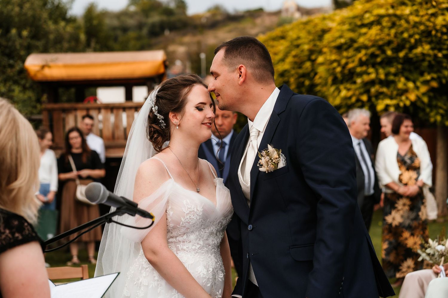 A tender moment between newlyweds at an outdoor wedding ceremony with yellow flowers in the background.