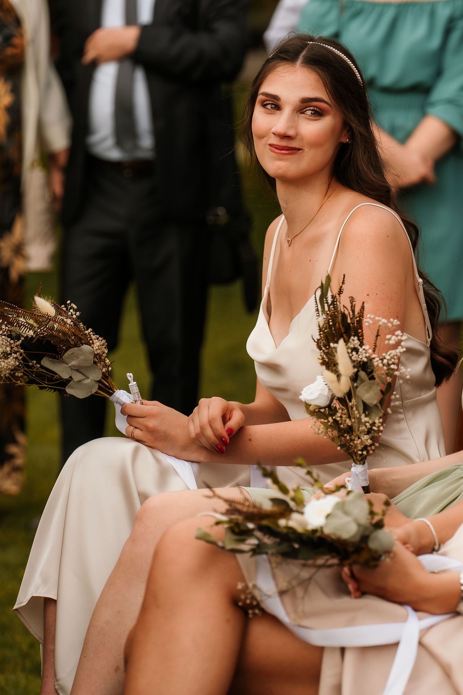 Bridesmaid in silk dress holds dried flower bouquet during outdoor wedding ceremony.