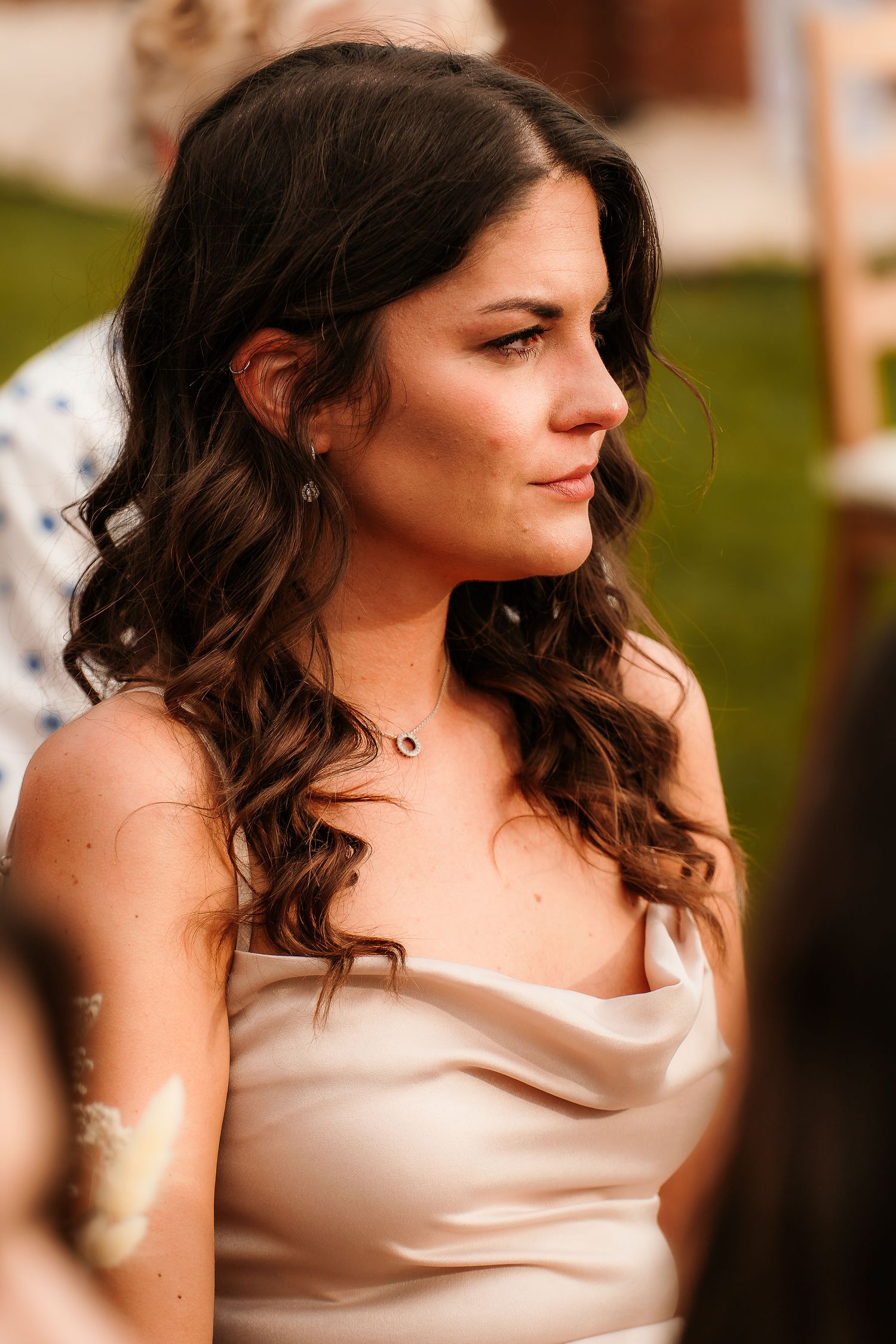 A woman with curled brunette hair in a satin dress photographed in warm evening light.