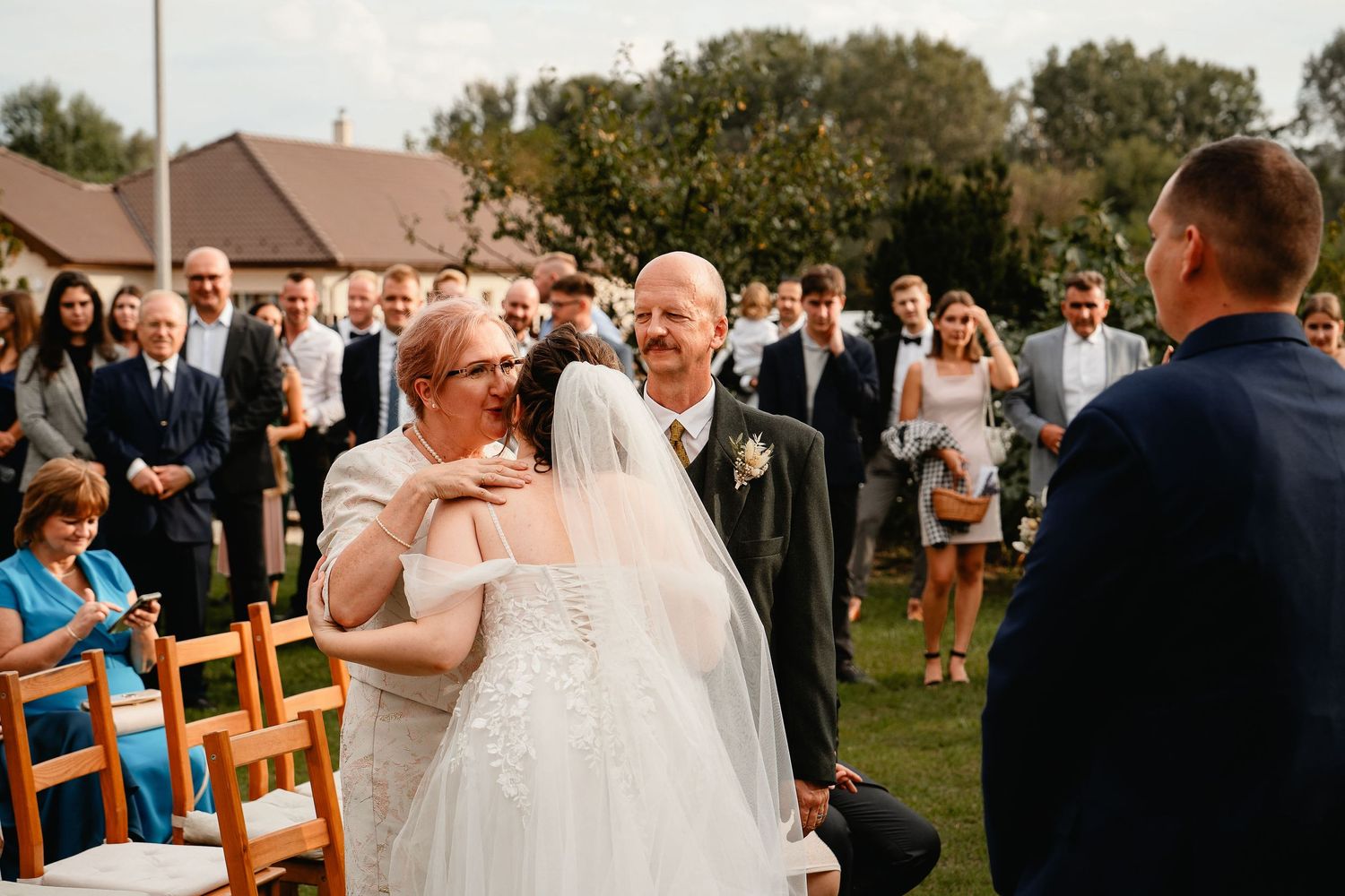 A joyful outdoor wedding ceremony with guests looking on from wooden chairs on the lawn.
