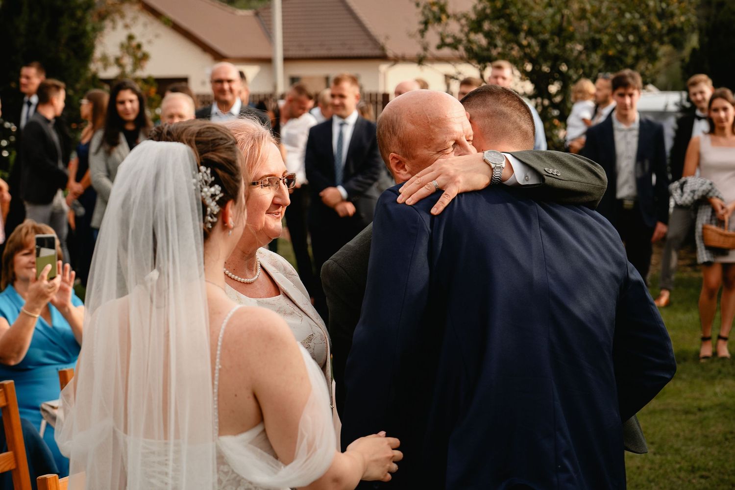 An emotional embrace during an outdoor wedding ceremony surrounded by guests.