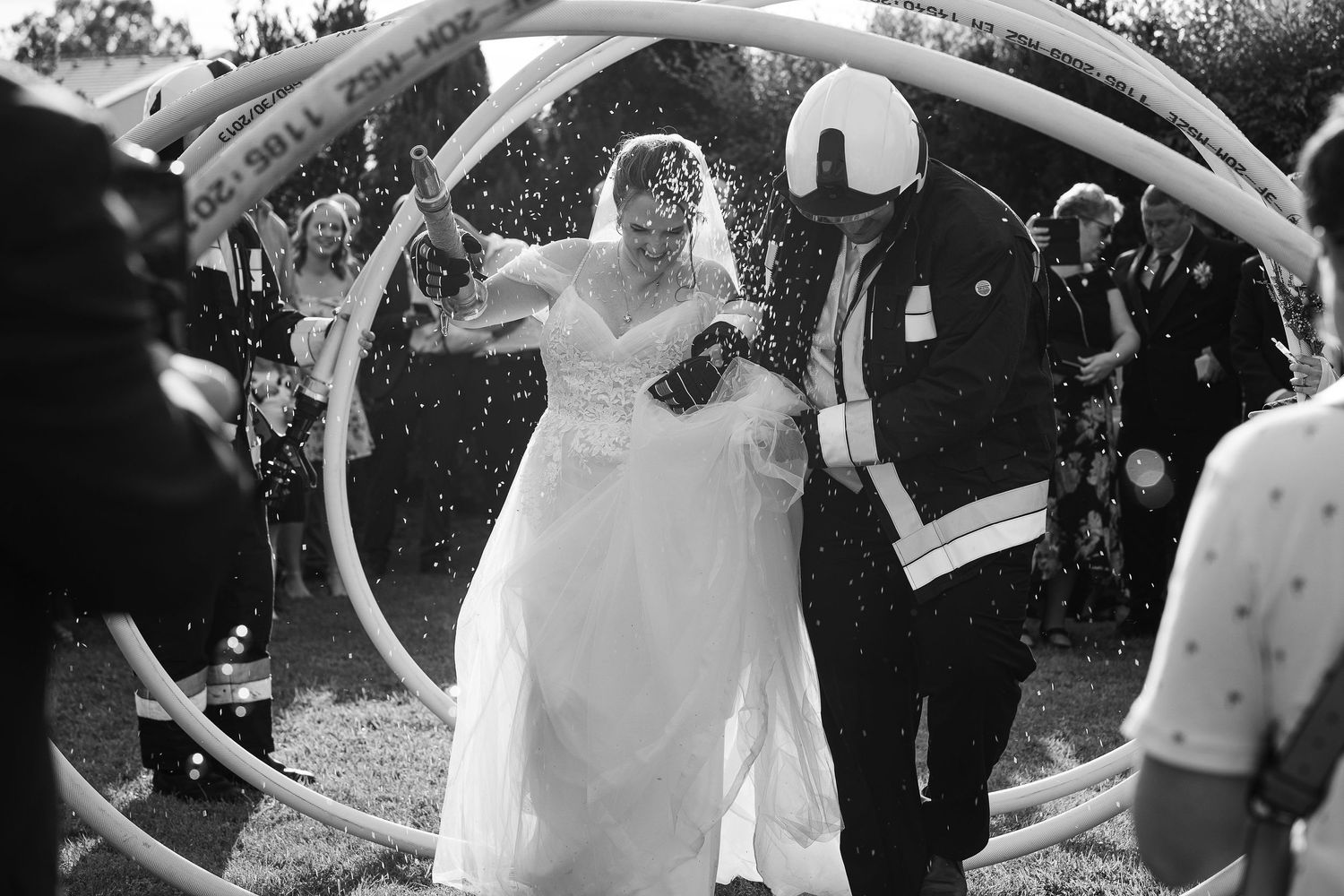 Couple passes through a water arch created by firefighters during outdoor celebration.