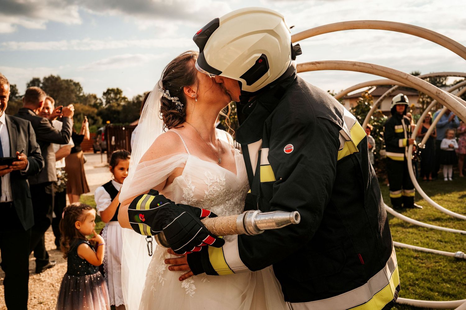 Couple shares romantic moment while one wears firefighter gear at outdoor wedding.