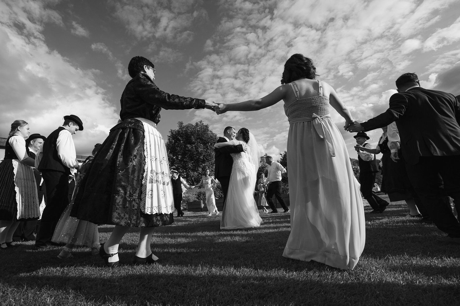 Dramatic black and white shot of traditional dancing in a circle at an outdoor wedding celebration.
