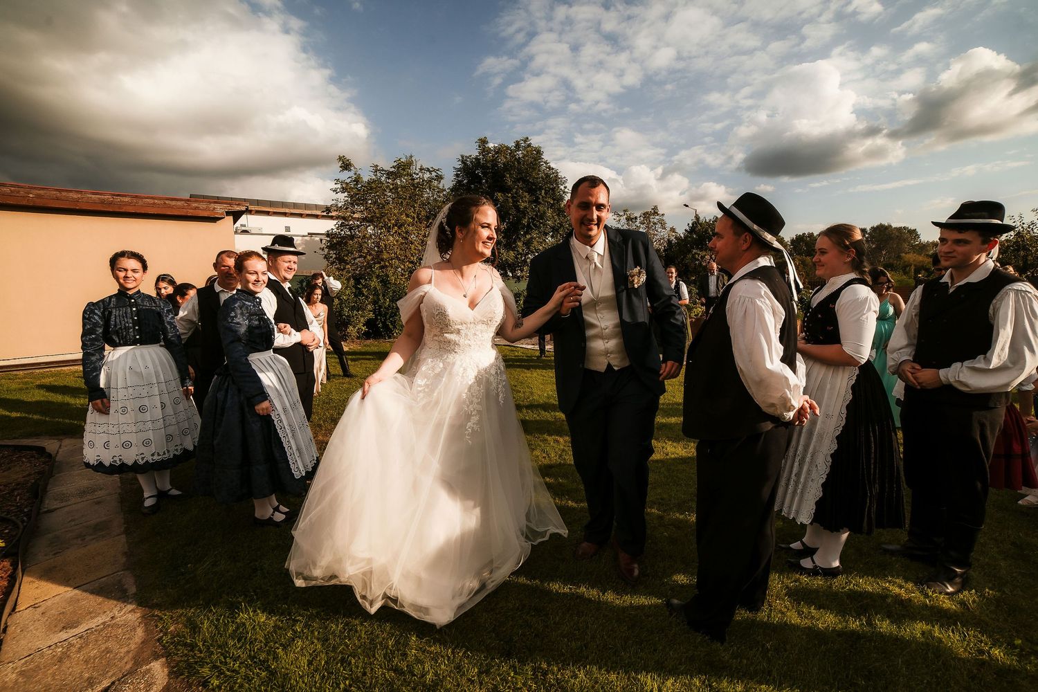 Wedding celebration featuring traditional folk dancers in period costumes under an evening sky.