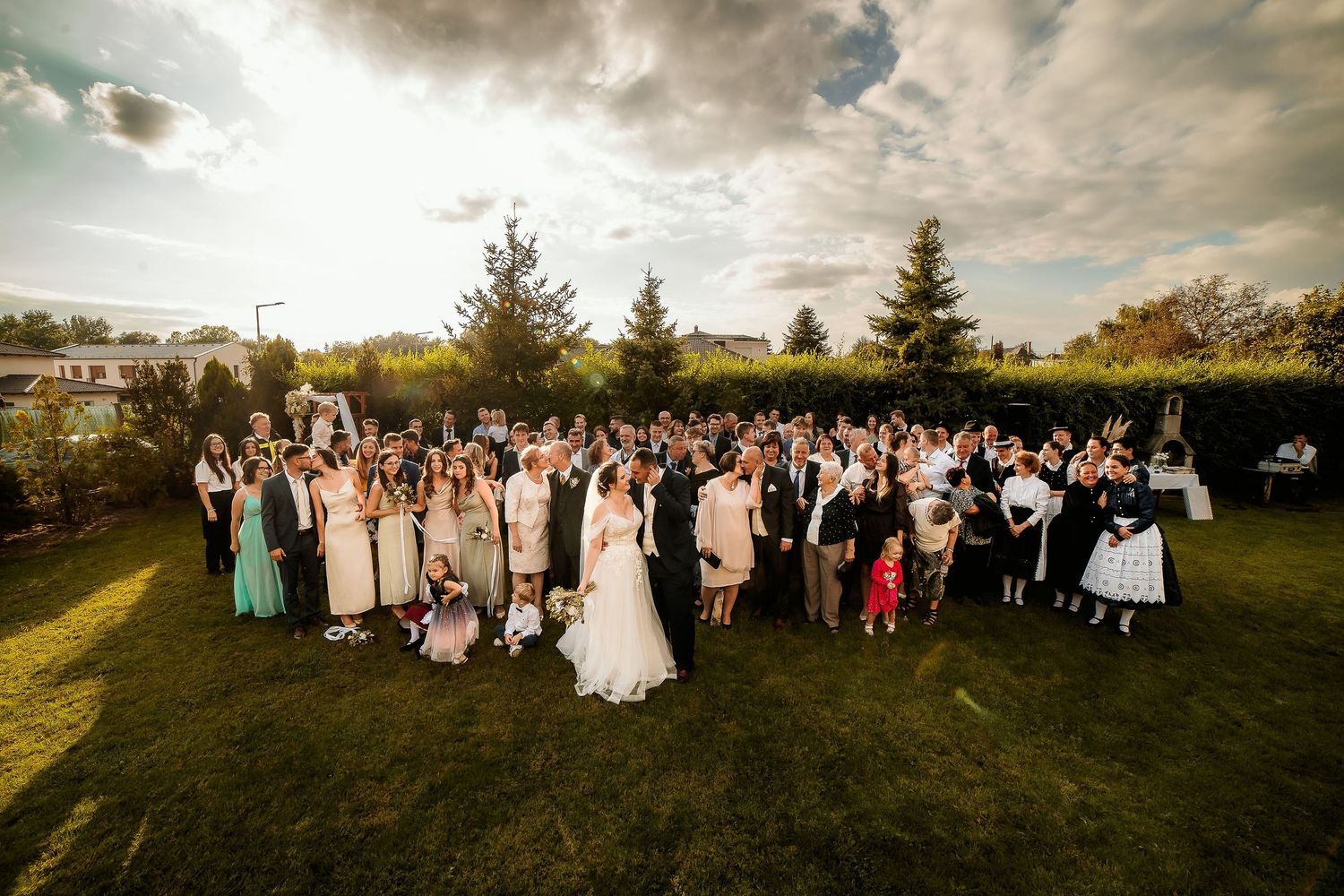 Large group wedding photo of guests in traditional folk costumes on a grassy hill.