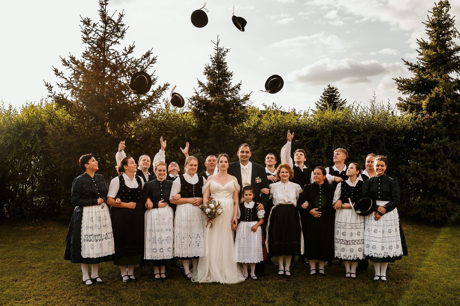 Wedding party members toss their hats in the air during a group photo outdoors.