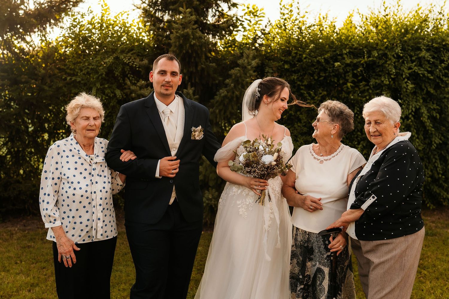 A wedding party gathers outdoors at sunset with family members sharing a joyful moment in the garden.