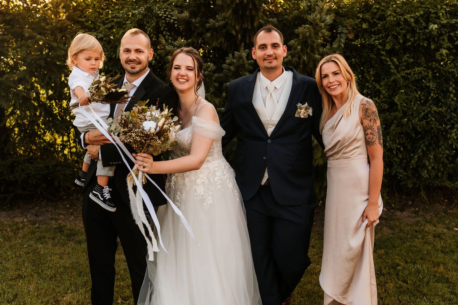 A wedding party poses together on grass during golden hour.