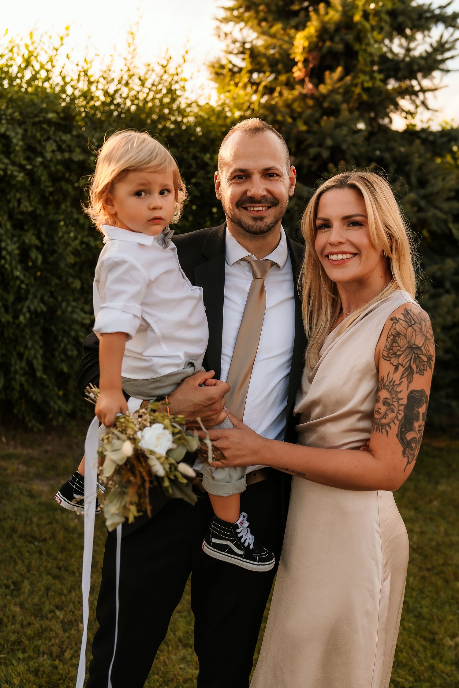 A stylish family poses together at sunset with greenery in the background.