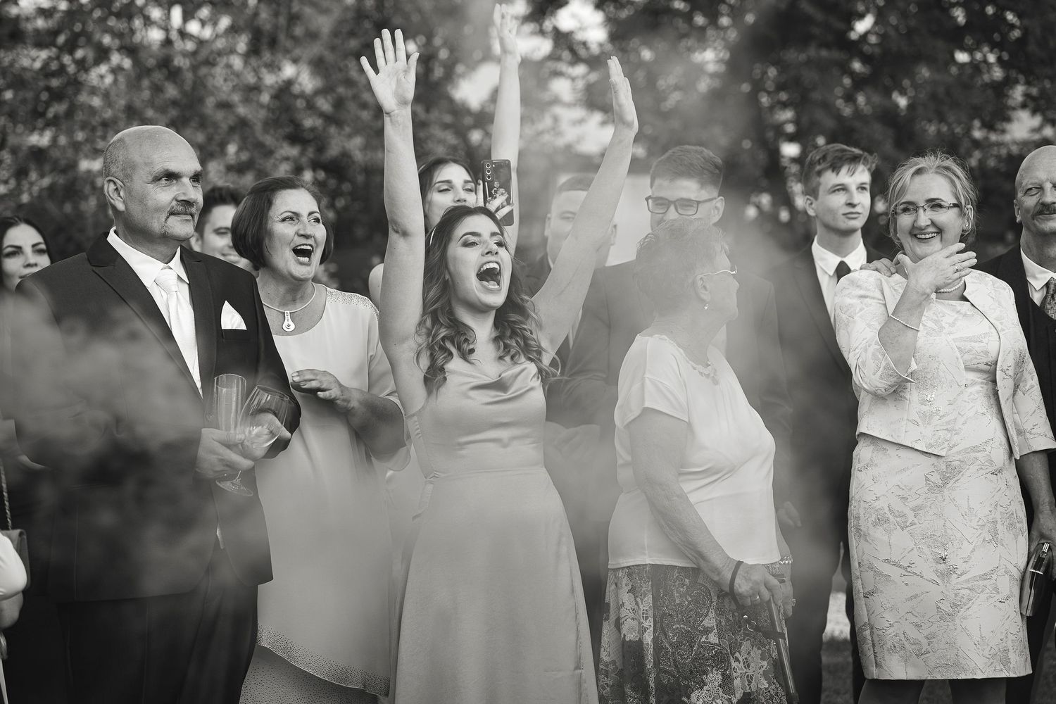 Wedding guests celebrate joyfully amid smoke effects at an outdoor reception.