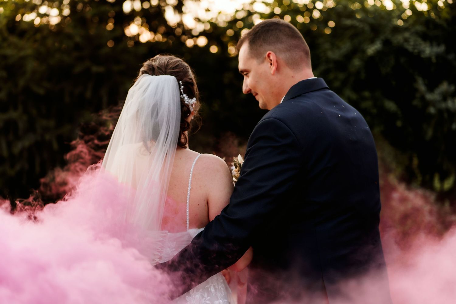 Newlyweds share a moment surrounded by pink smoke during their wedding photoshoot.