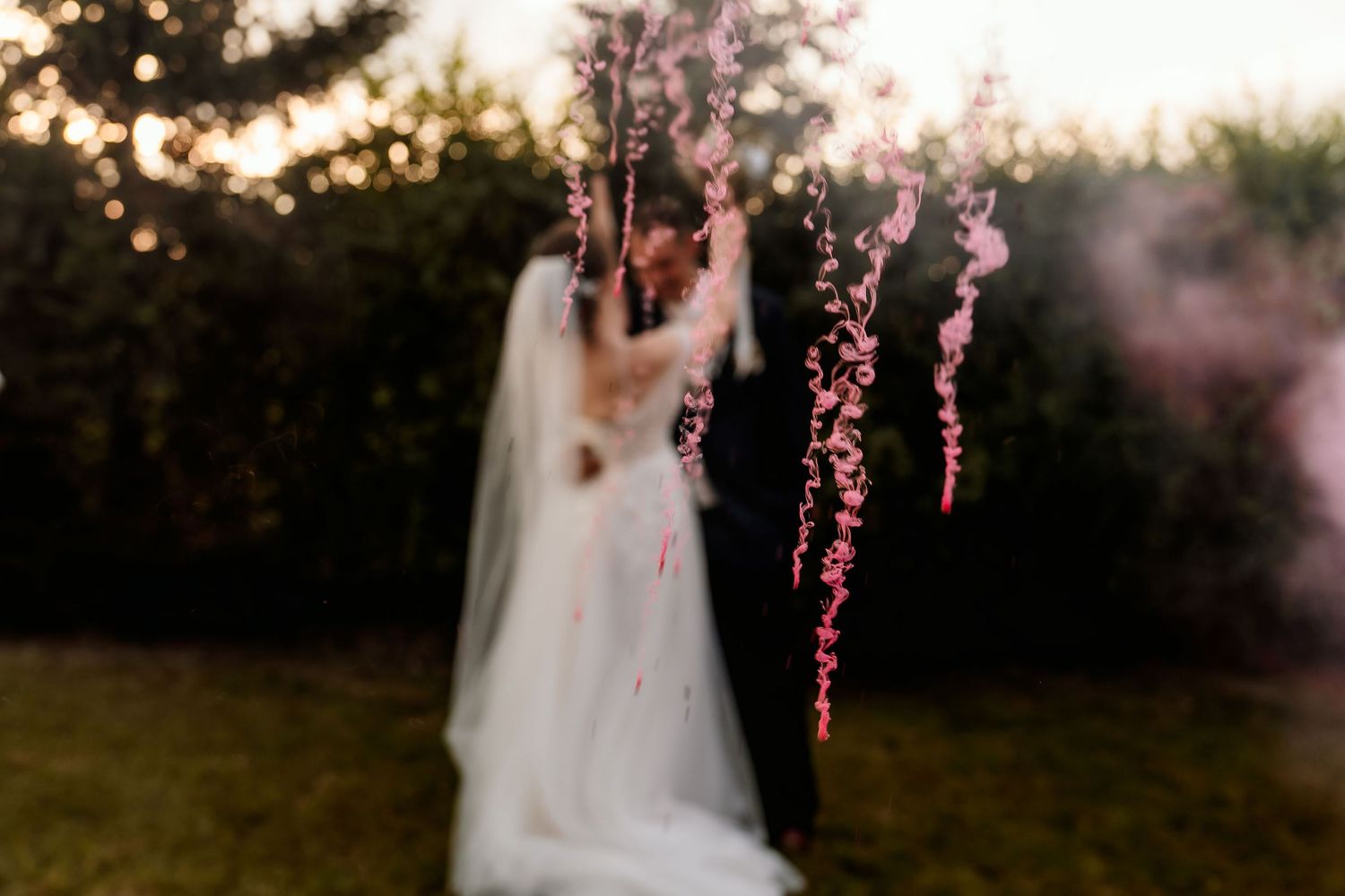 Dreamy silhouette of a bride with floating pink floral details at sunset.