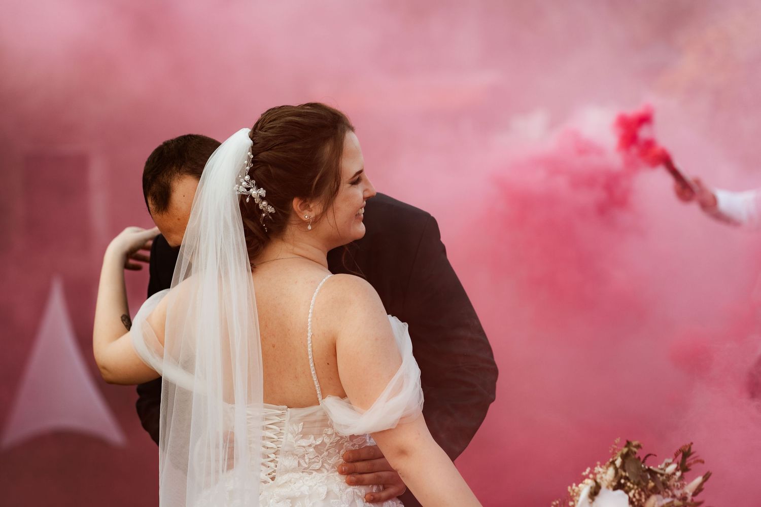 A couple embraces during their wedding celebration surrounded by pink smoke.