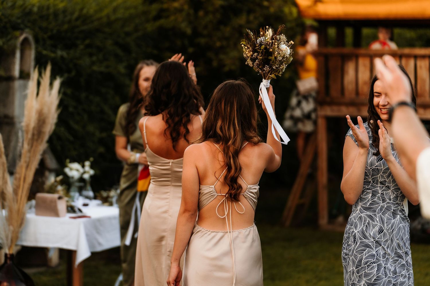 Wedding party members in neutral dresses gather during outdoor reception festivities.