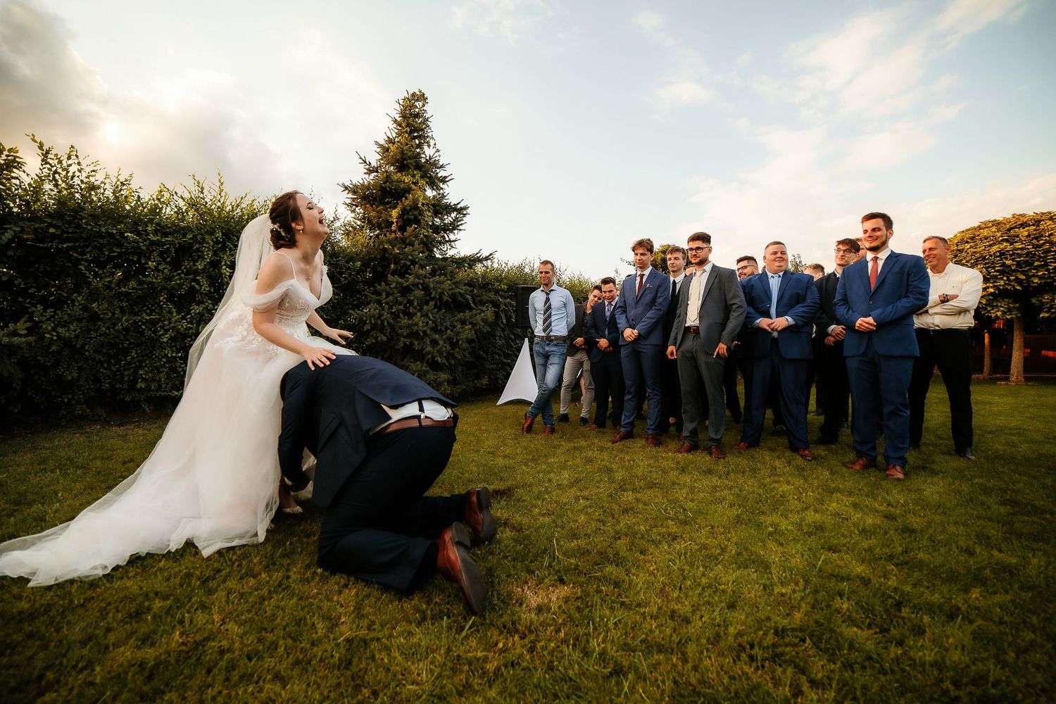 Wedding couple performs special ceremony moment with groomsmen watching on lawn.