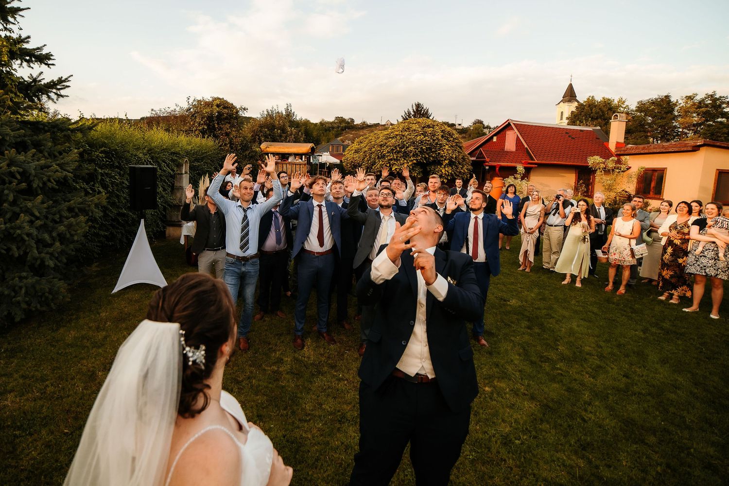 Wedding guests and groomsmen raise their arms in celebration on a lawn.