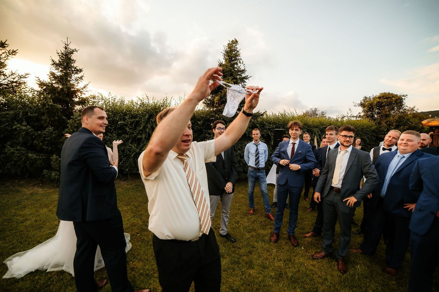Playful wedding celebration moment with guests on lawn at sunset.