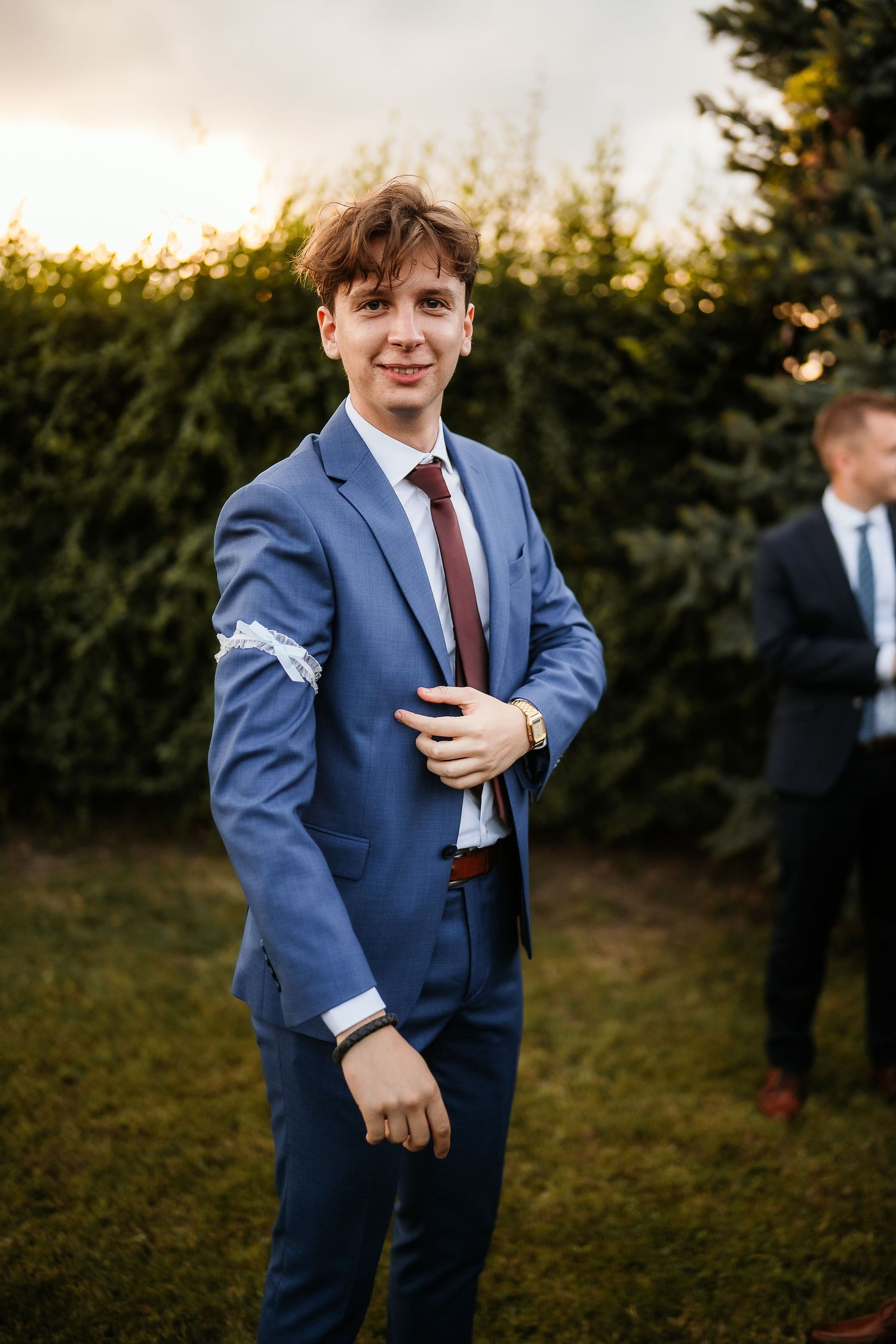 Groomsman in blue suit with burgundy tie poses during outdoor wedding reception.