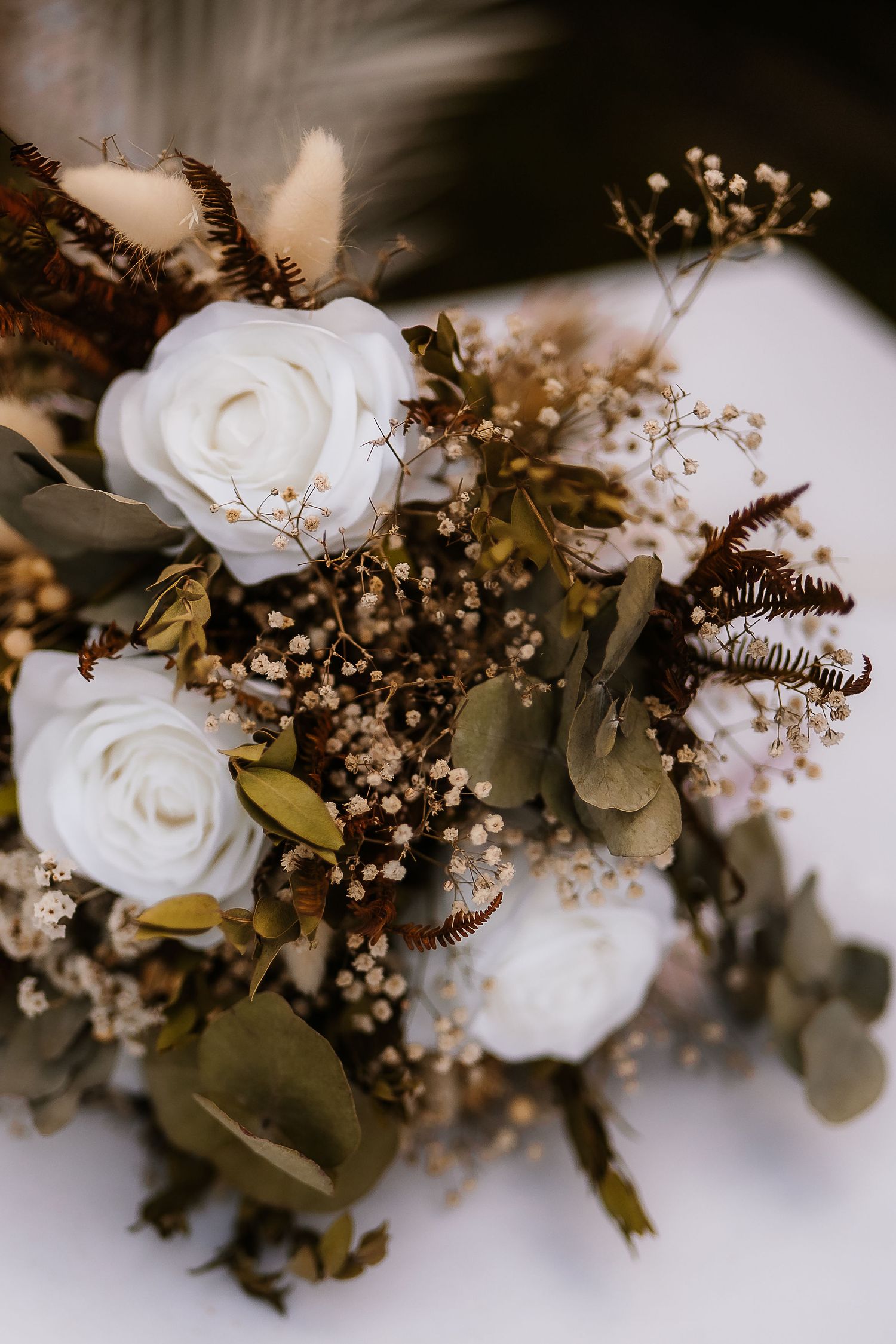 Elegant wedding bouquet with white roses, baby's breath, and eucalyptus leaves in a moody lighting setting.