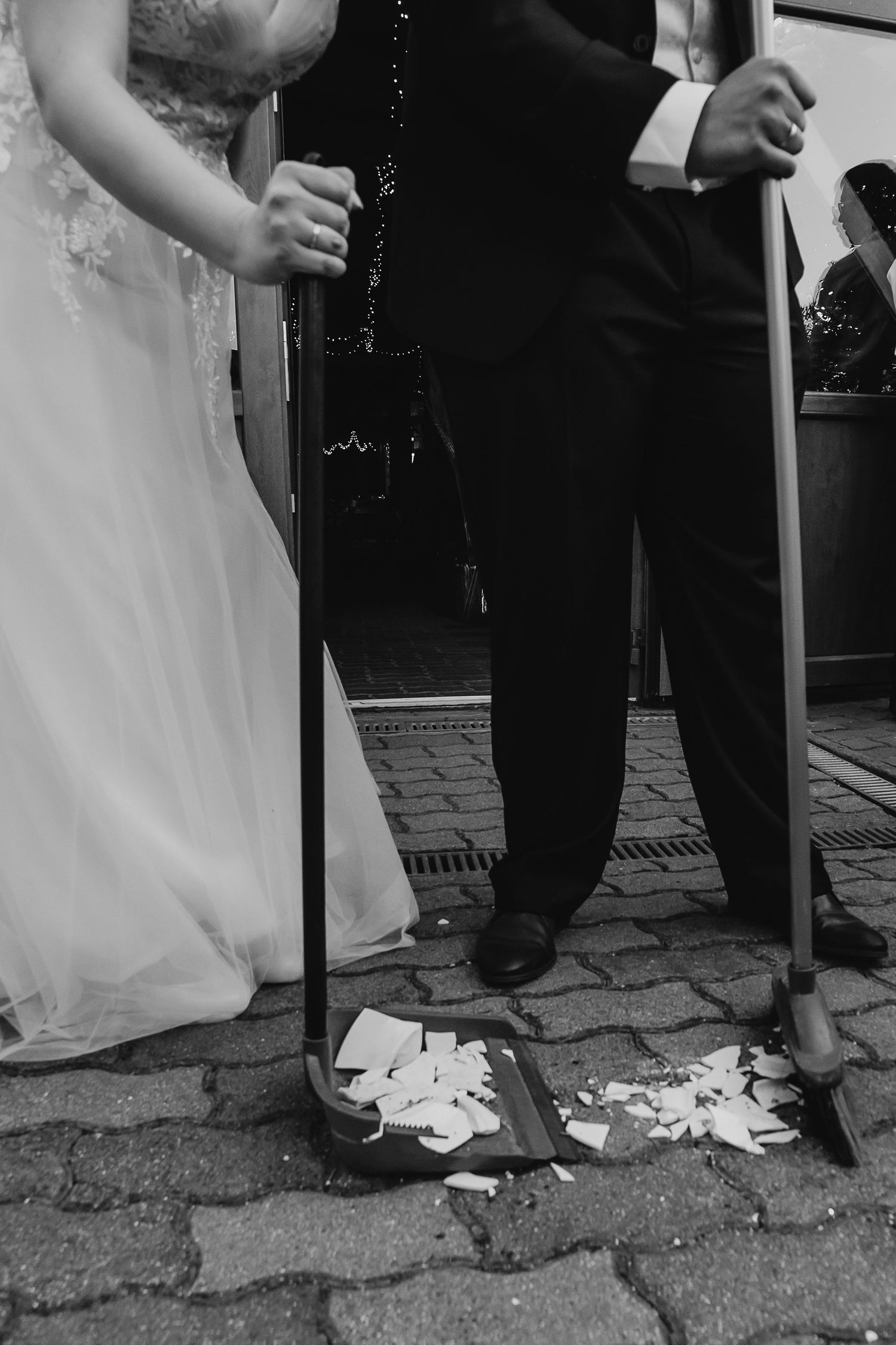 Black and white detail shot of formal attire and broken items on brick pavement.