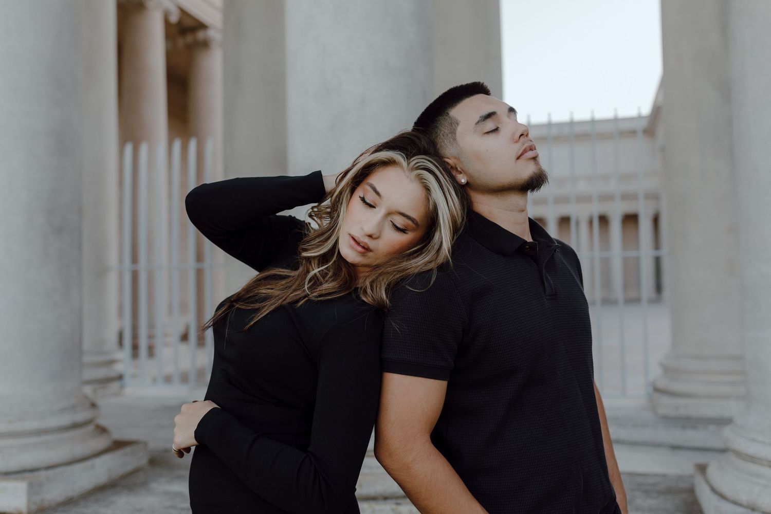 A couple, wearing all black, closes their eyes and leans against each other in this editorial photo.