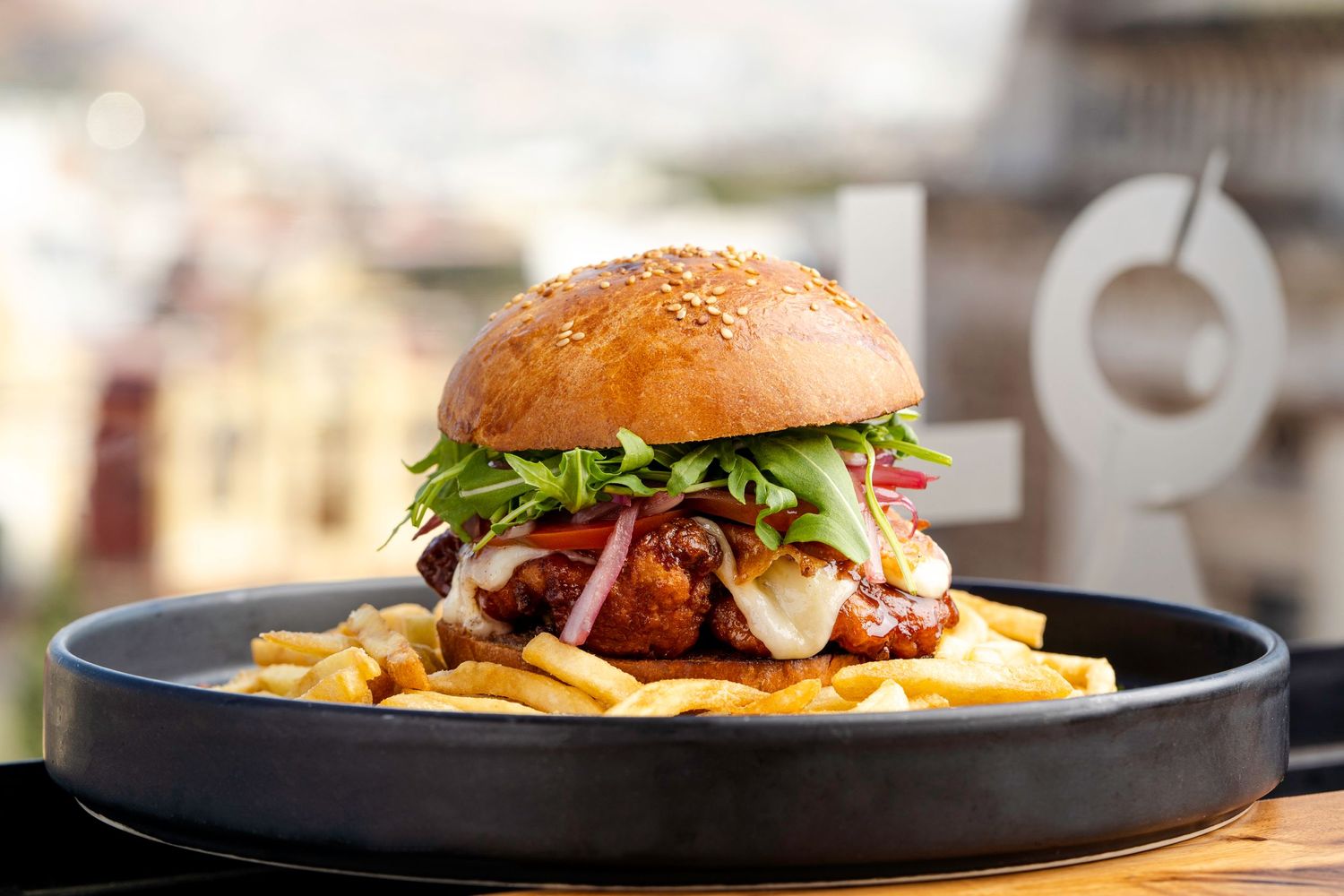 Series of gourmet hamburgers with fries served on black plates in restaurant setting.