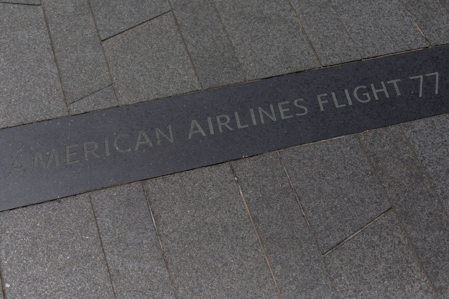 Engraved memorial text for American Airlines Flight 77 on gray stone surface.