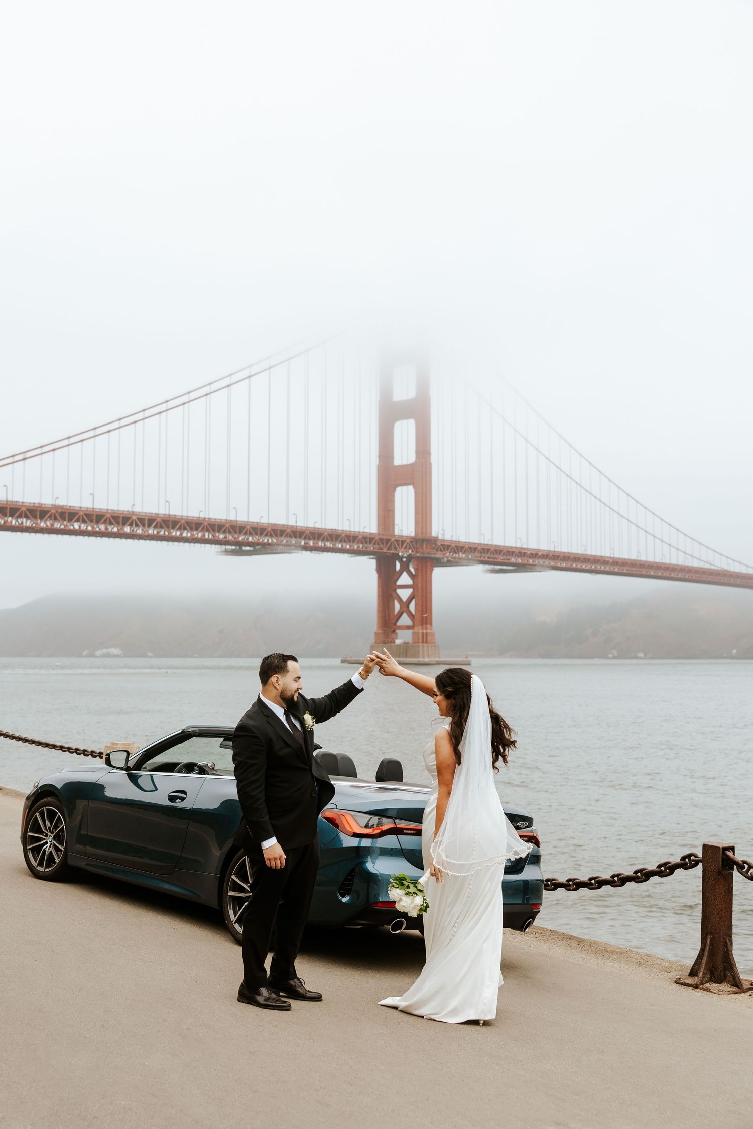 groom and bride dancing in front of a convertible car with the Golden Gate Bridge in the background on their elopement day in San Francisco
