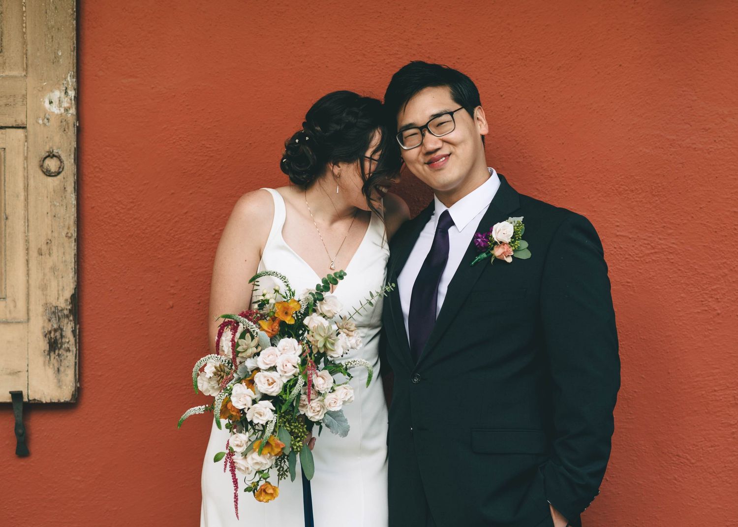 Bride and groom in front of the red Adobe walls at Cooper Molera in Monterey.