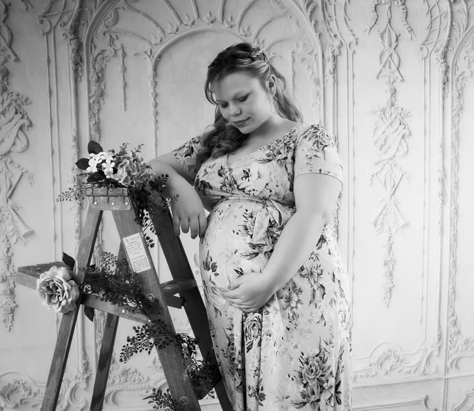 Black and white maternity portrait with floral dress and vintage architectural backdrop.