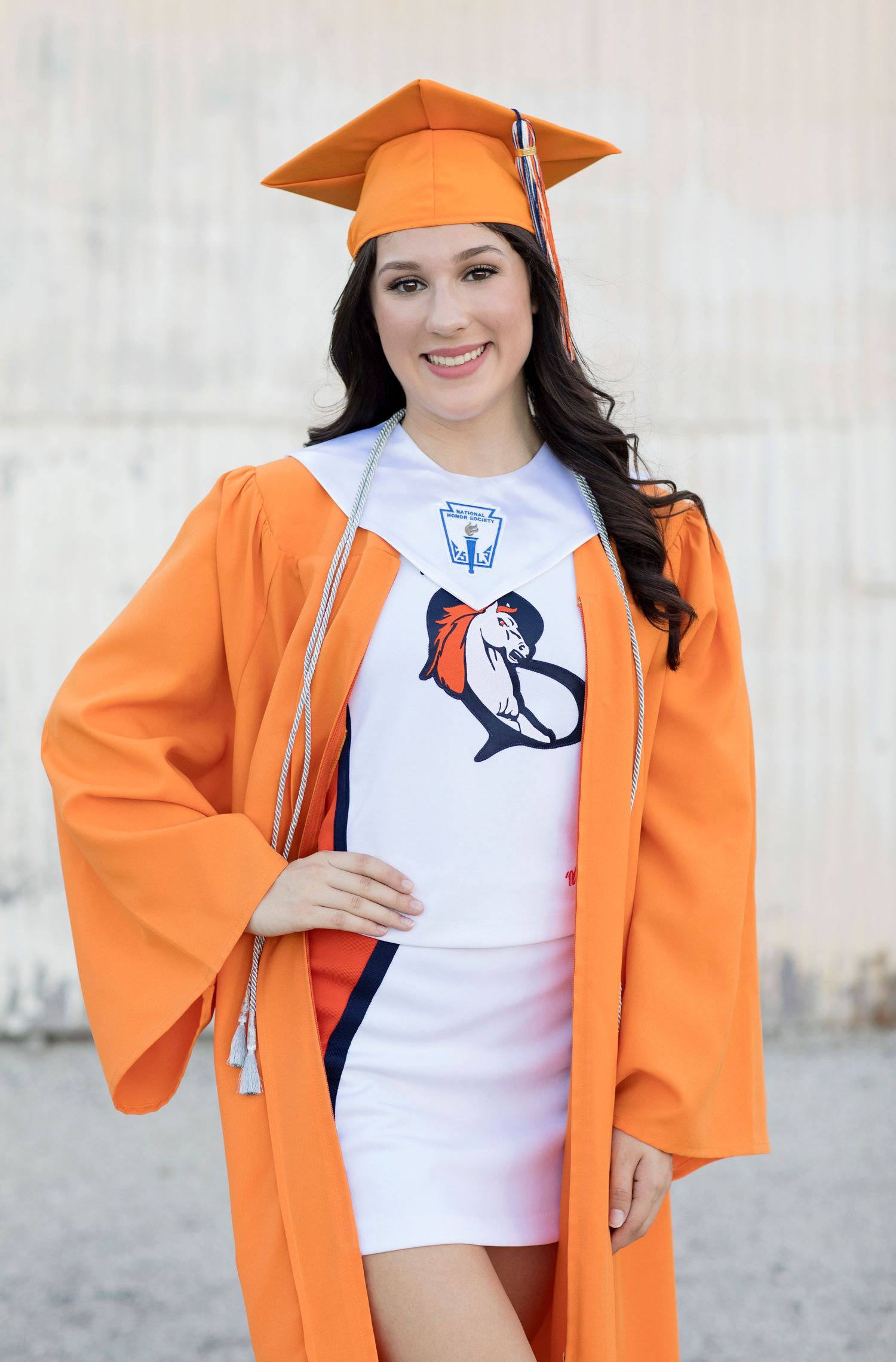 Graduate in orange cap and gown displaying university mascot shirt.
