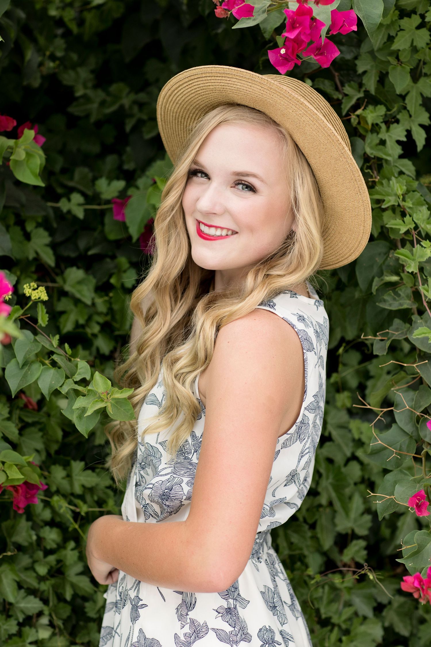 Joyful outdoor portrait with straw hat and floral dress against pink flowers.