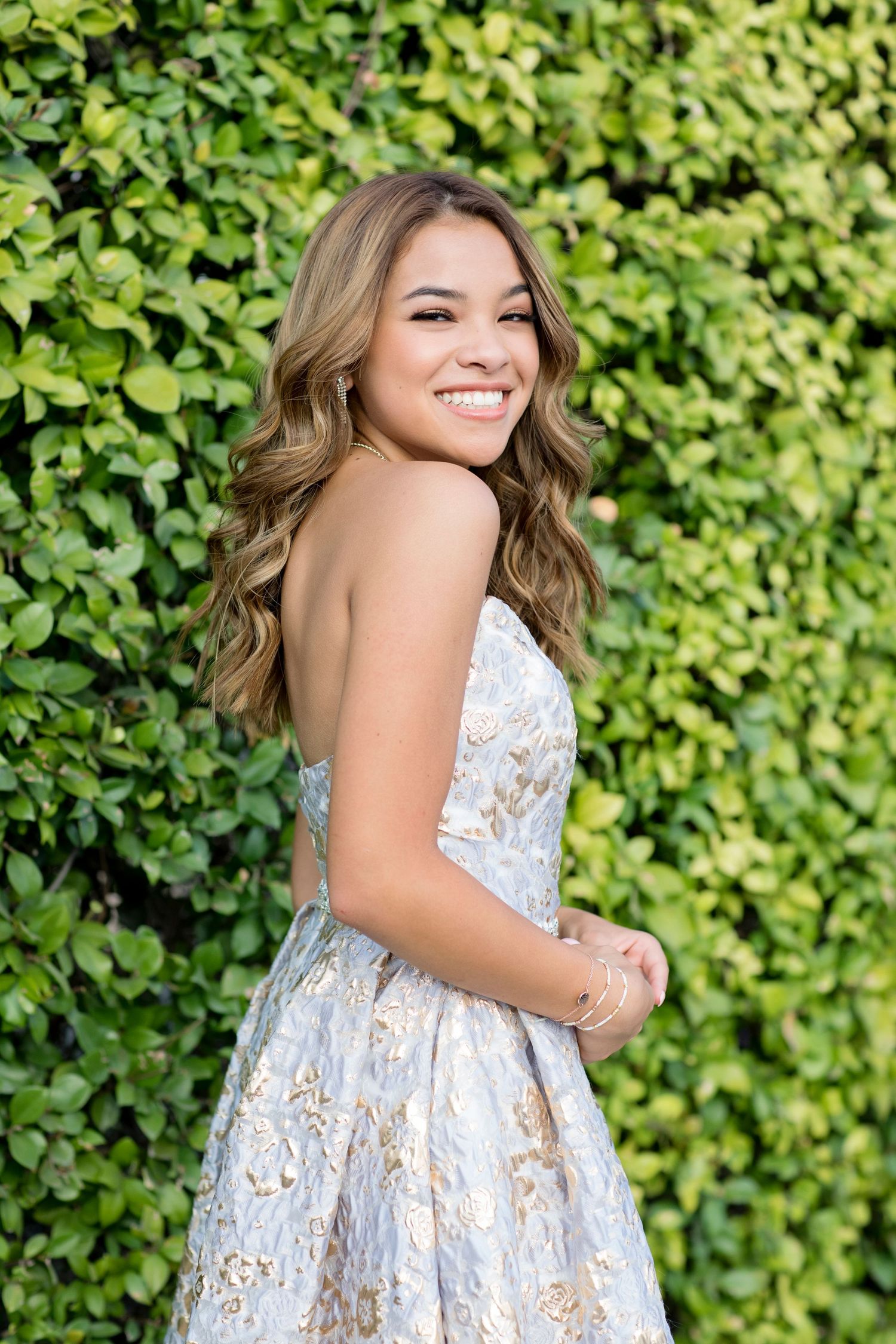 Elegant white and gold floral brocade dress photographed against lush green garden backdrop.