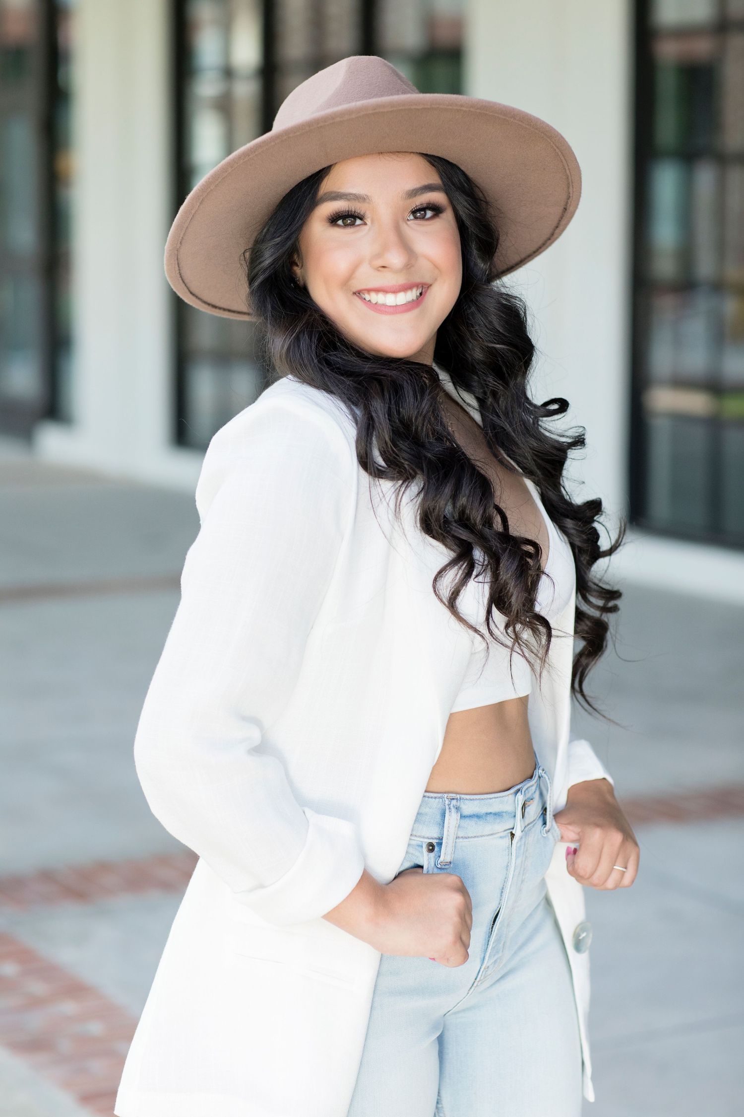 Chic street style outfit with tan hat, white blazer and light denim against urban backdrop.