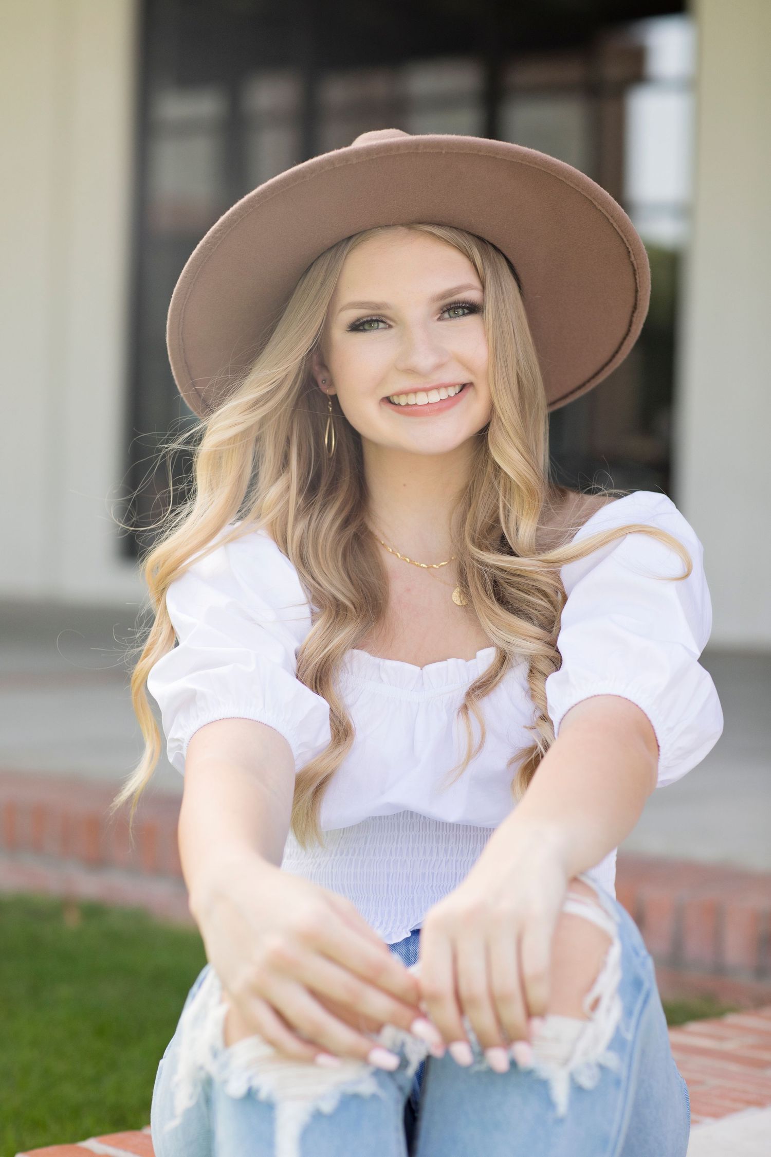 Outdoor portrait wearing a white peasant top, wide-brim tan hat and distressed jeans.