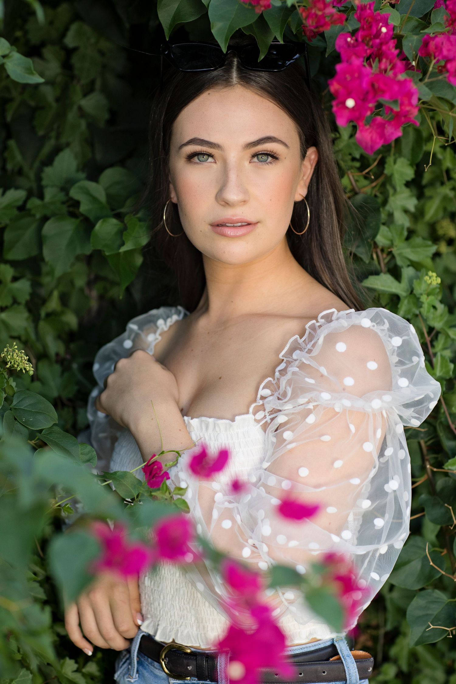 A feminine portrait against pink bougainvillea flowers wearing a sheer white romantic top with puff sleeves.