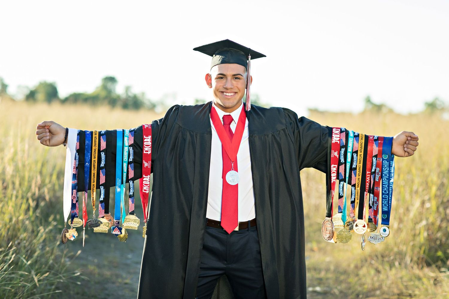 Graduate wearing black gown displays collection of academic medals outdoors.