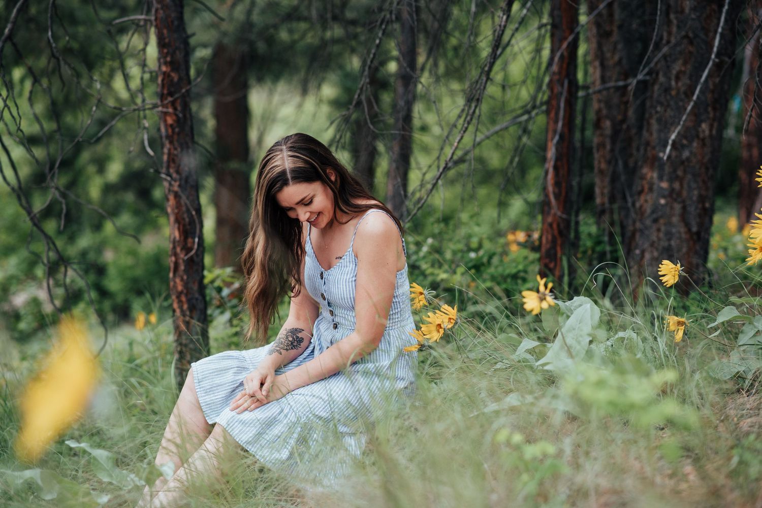Woman in light blue dress sitting thoughtfully in a forest meadow with yellow flowers.