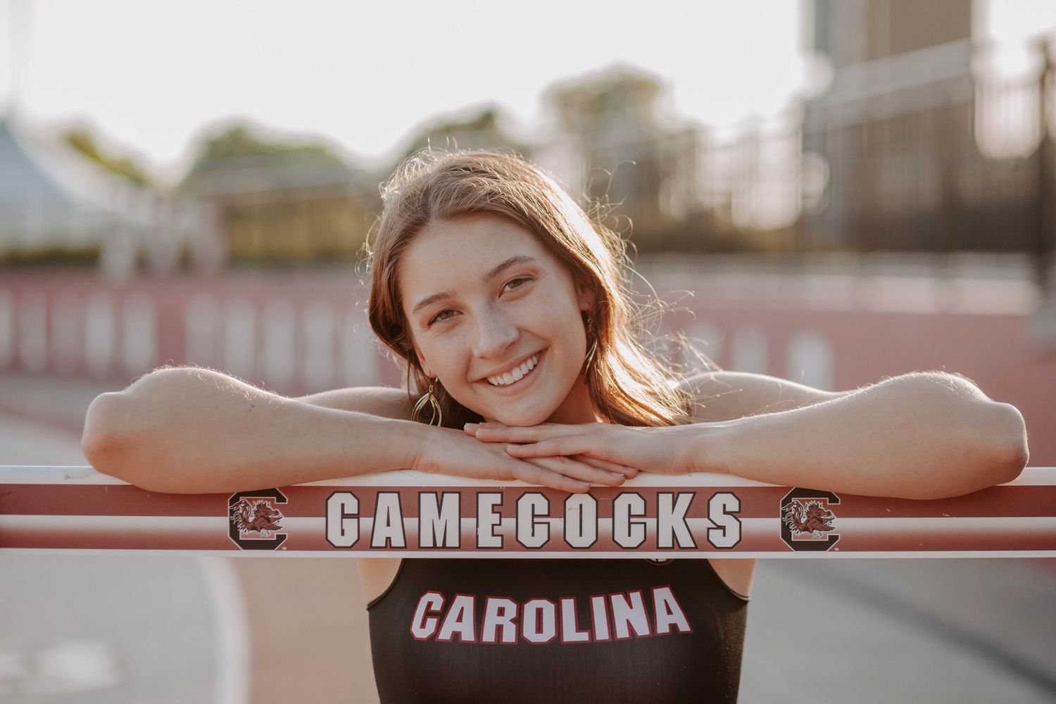 Smiling student athlete poses with her university hurdle in the track and field facility.