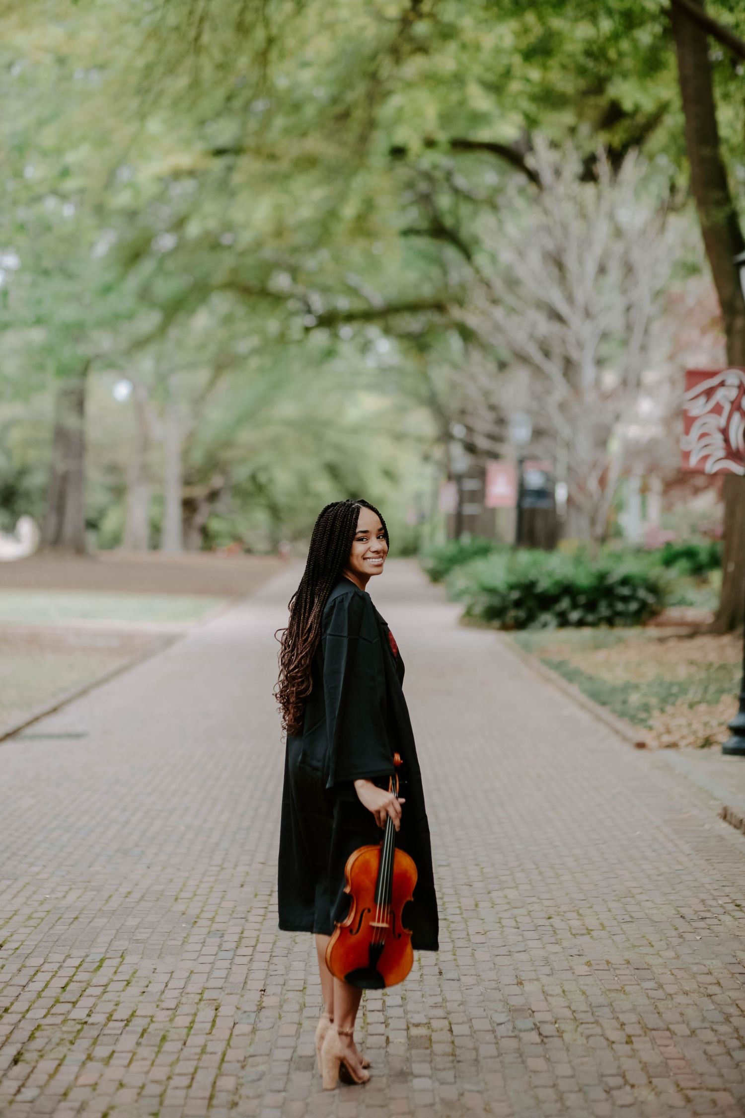 College graduate photos taken of a music major and her viola walking down a picturesque path on campus.