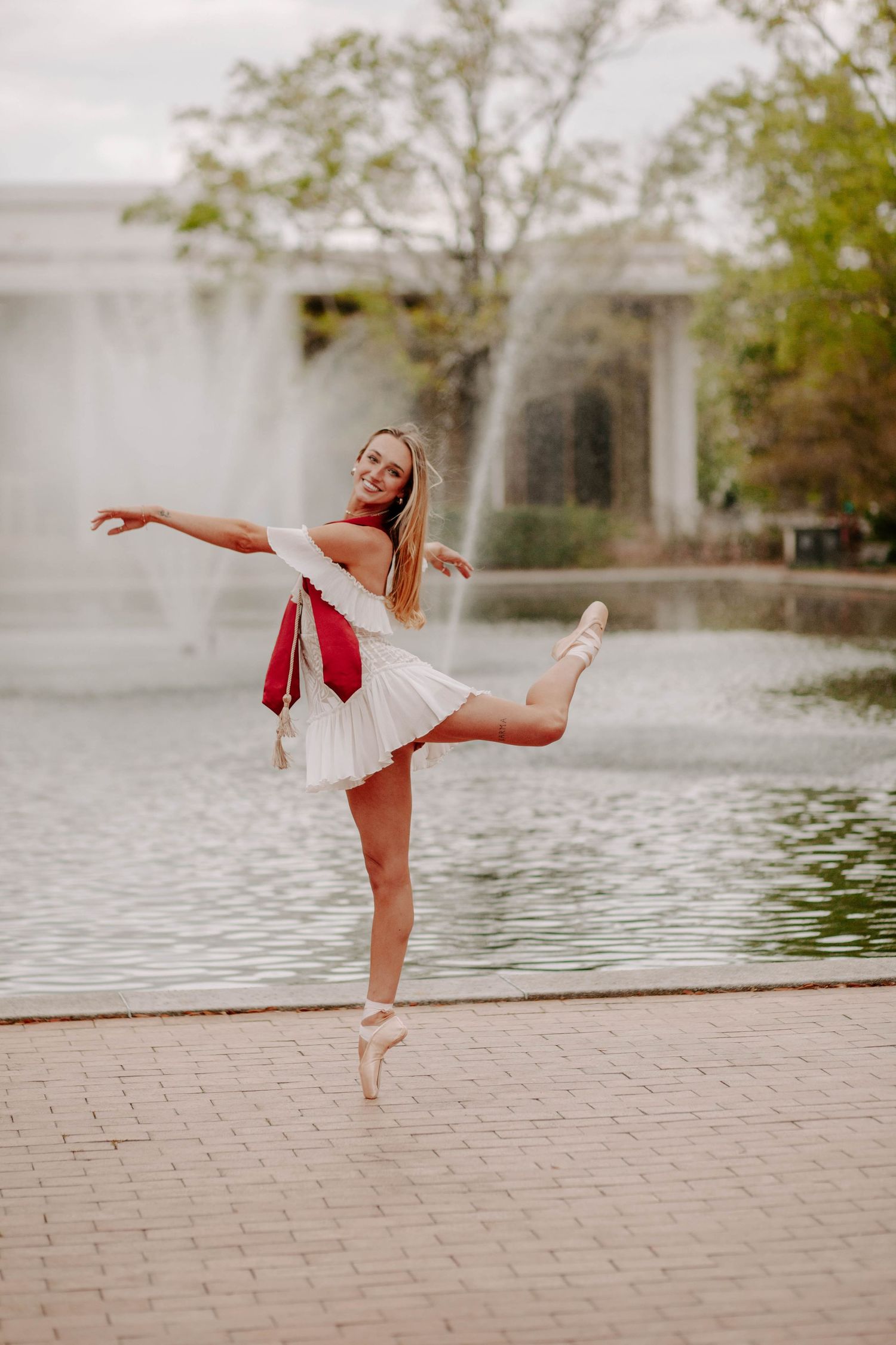 College graduate strikes ballerina pose in her pointe shoes on her campus.