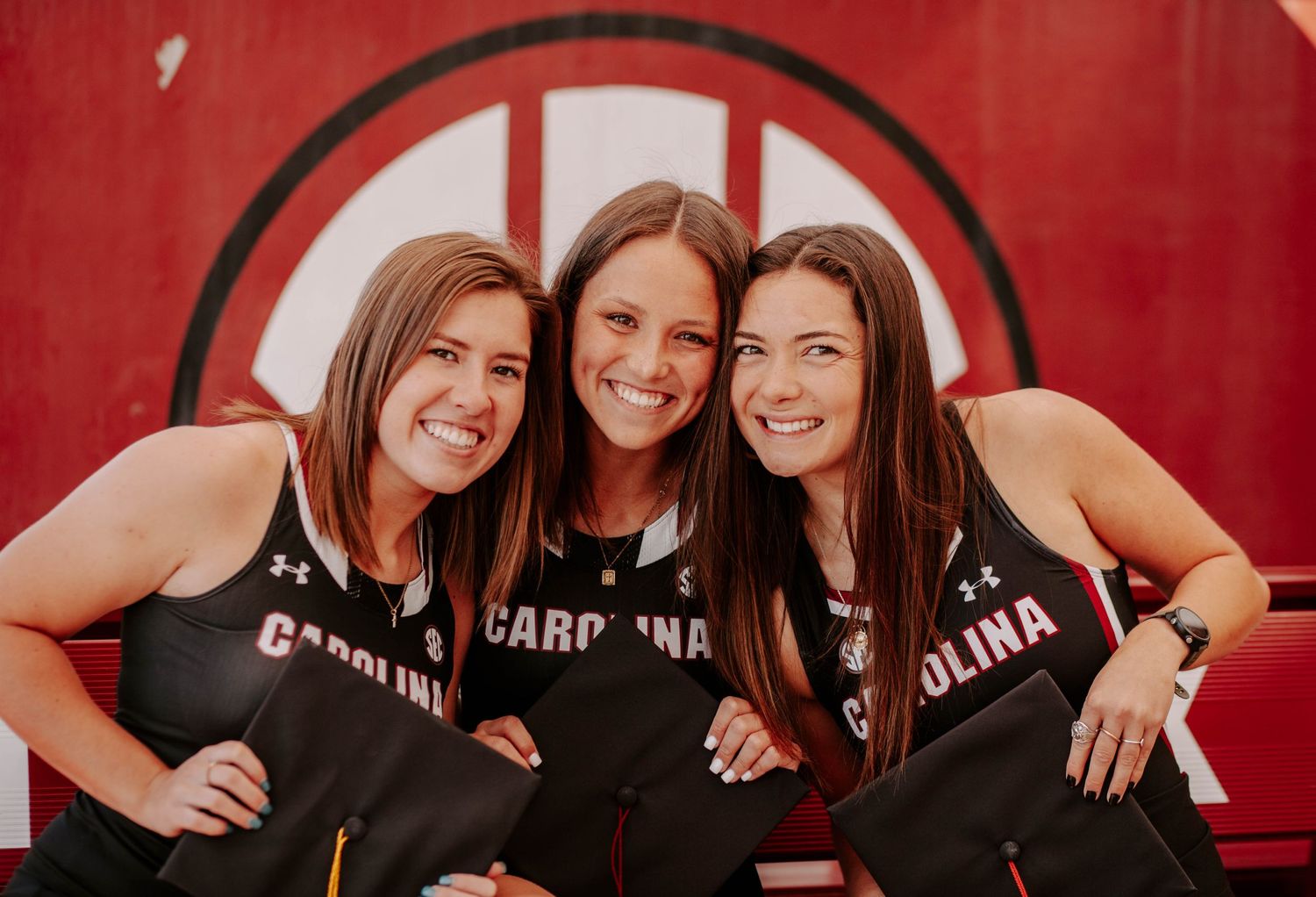 College student-athlete graduates and friends lean in together and smile.