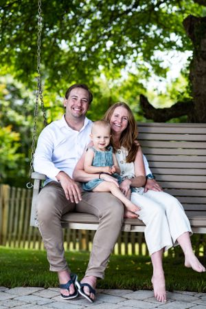 Family relaxes together on wooden porch swing in garden setting.