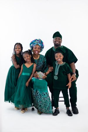 Family of five wearing coordinated green traditional African attire poses together against white background.