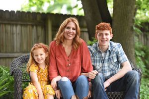 A casual outdoor family portrait on a wicker bench in a backyard garden setting.